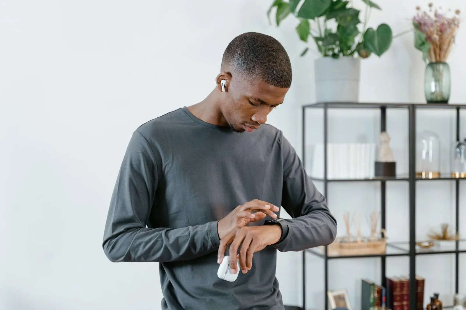 A Black man stands in a bright modern home, calmly reviewing his health data on a smartwatch, engaged and in control of his care.